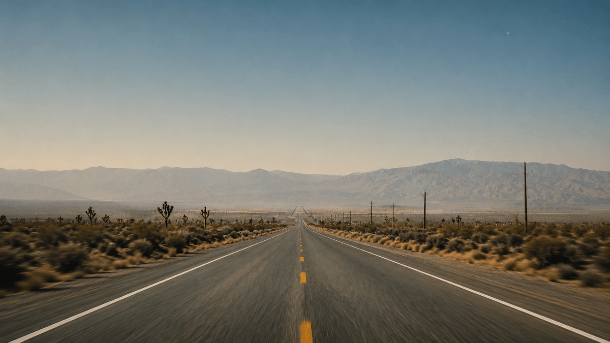 A desert highway stretching toward the horizon under a vast pale sky.
